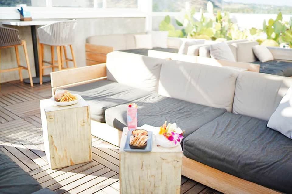 Rooftop lounge area with white cushioned seating, wooden tables, and scenic overlook