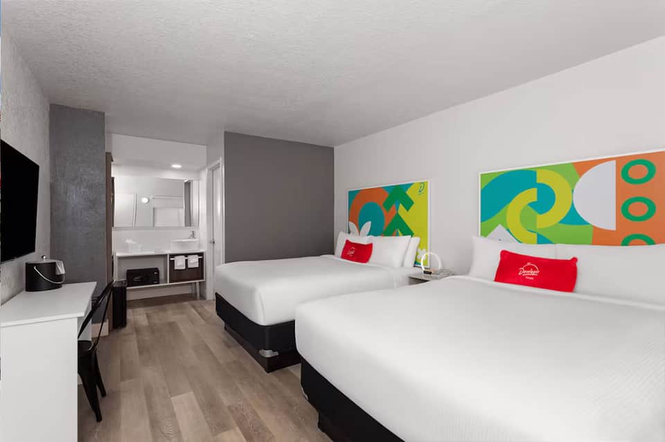 Colorful modern hotel room with two queen beds, bright artwork, and ensuite bathroom