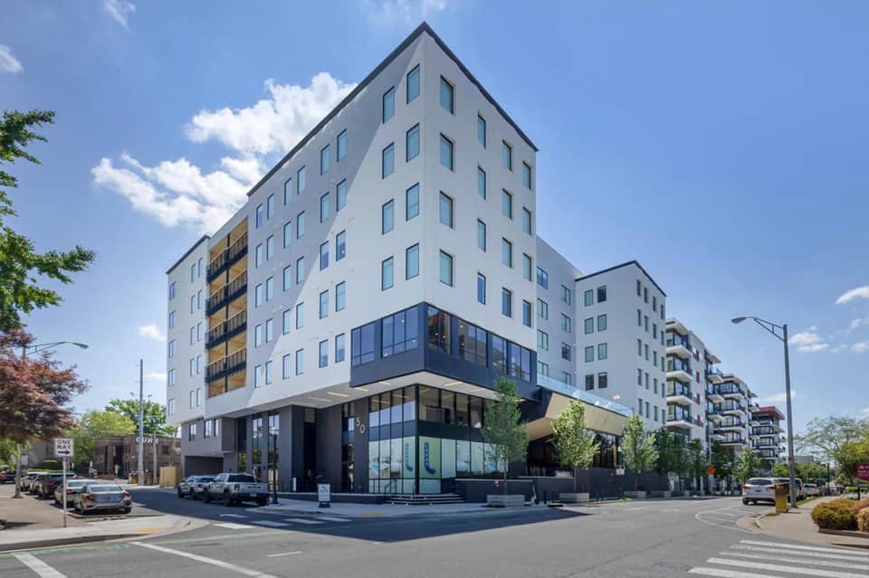 Modern white multi-story apartment building with blue-trimmed ground floor commercial space on city street