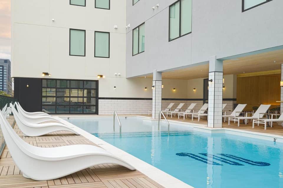 Modern indoor swimming pool with loungers, white columns, glass doors opening to outdoor terrace, contemporary architecture