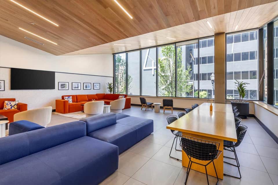 Contemporary lounge with wooden ceiling, blue modular seating, orange accents, and floor-to-ceiling windows