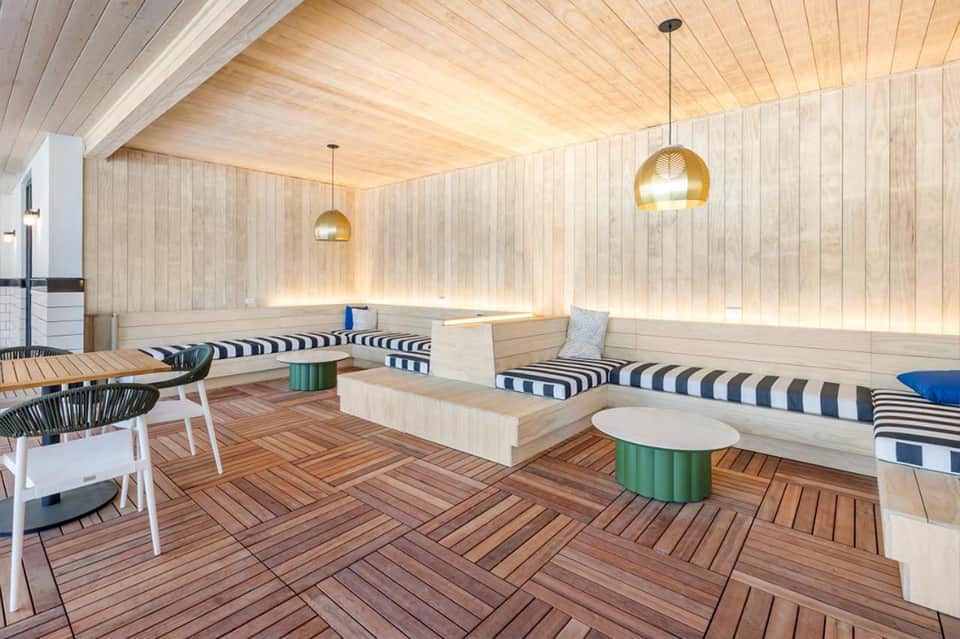 Modern sauna lounge with wooden walls, built-in benches, pendant lighting, and striped cushions