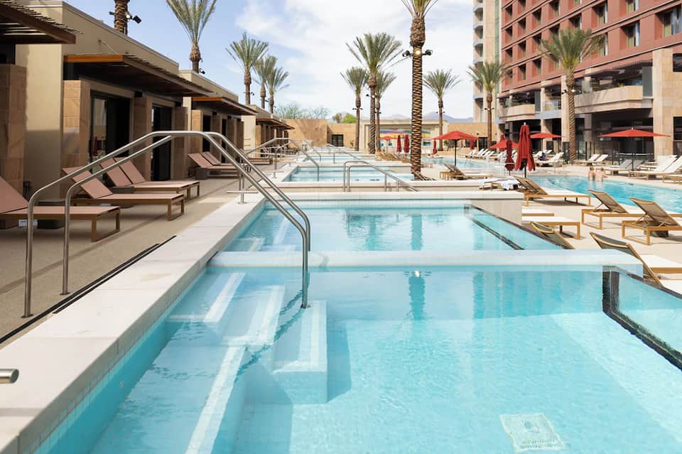 Resort lap pool with clear turquoise water, lounge chairs, palm trees, and modern architecture