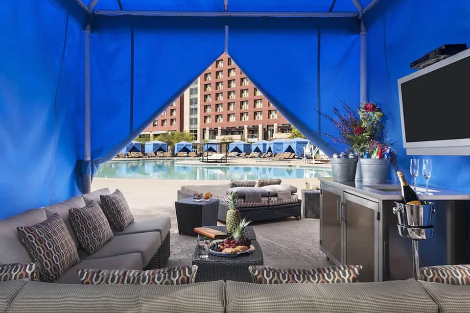 Luxury poolside cabana with blue canopy, modern seating, view of beachfront resort and turquoise pool