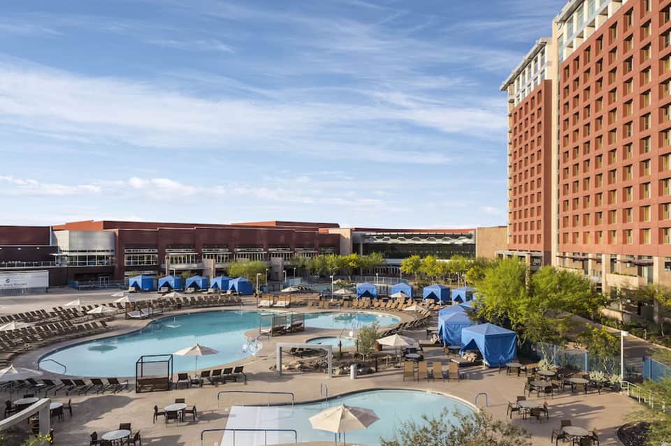 Resort pool area with blue umbrellas, loungers, and brick building against cloudy sky