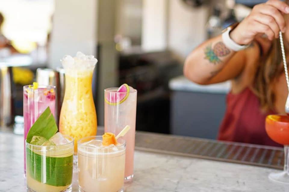 Colorful tropical cocktails on a bar counter with a bartender in the background