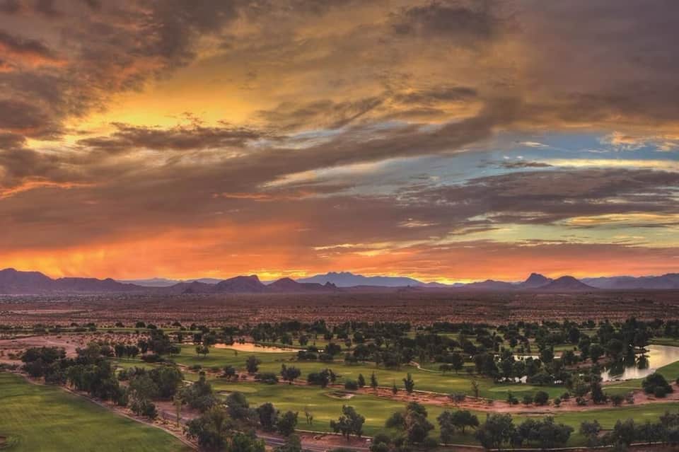 Dramatic sunset over wide valley landscape with mountains, green fields, and winding river