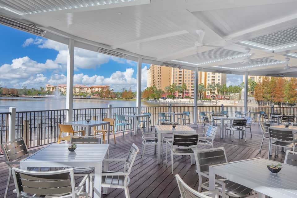 Waterfront covered patio with white pergola, gray and white chairs, tables, and lake view