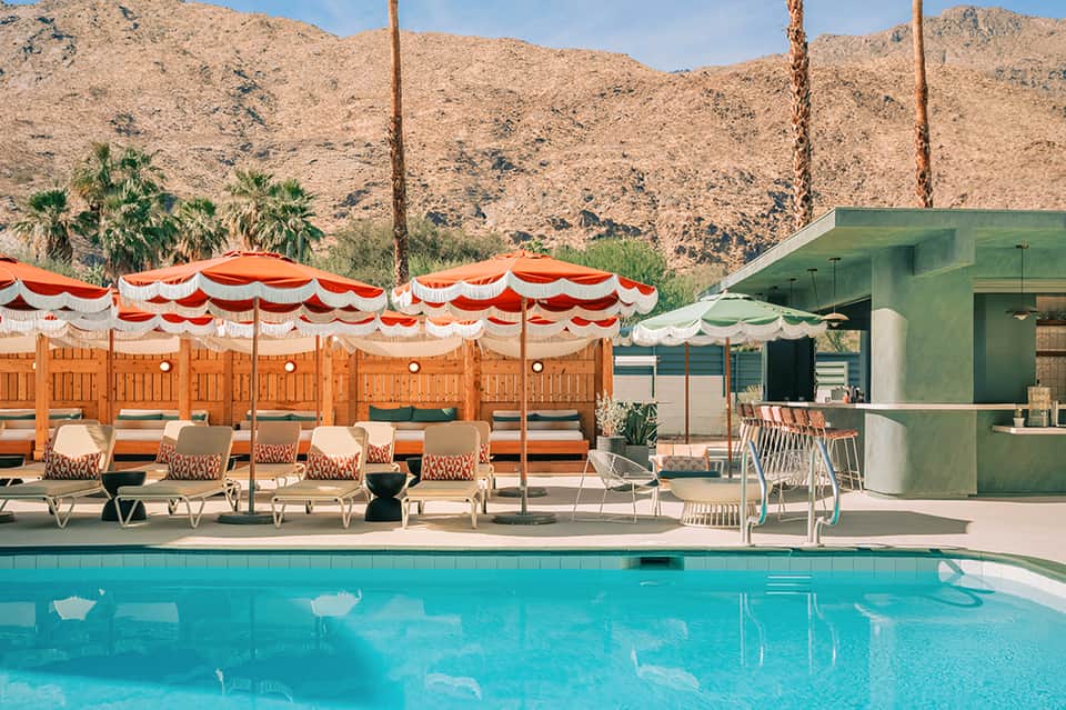 Vintage pool with red and white striped umbrellas, loungers, and mid-century modern poolside cabana