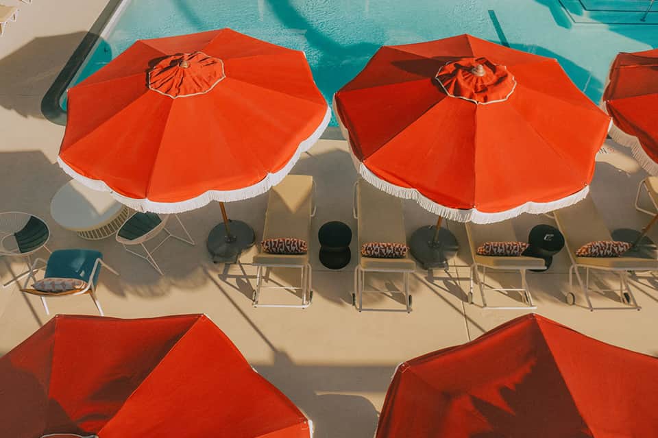 Overhead view of bright orange and white beach umbrellas with lounge chairs beside a turquoise pool