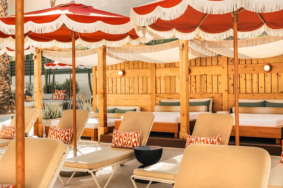 Luxury beach club with wooden cabanas under orange and cream striped awnings and cushioned seating