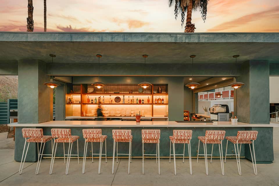Modern outdoor bar with teal counter and coral patterned stools at dusk