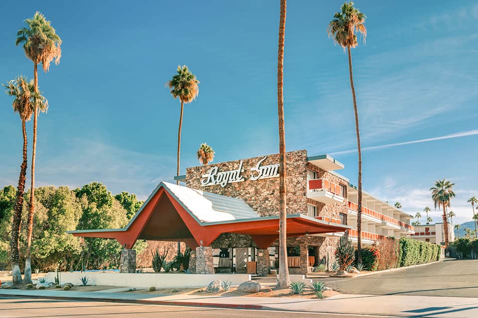 Retro Royal Inn hotel exterior with red canopy, stone facade, and tall palm trees