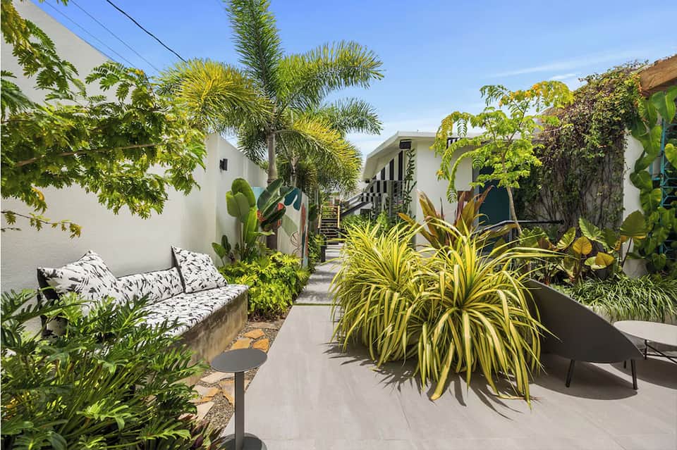 Tropical resort courtyard with white modern buildings, lush green plants, and seating areas
