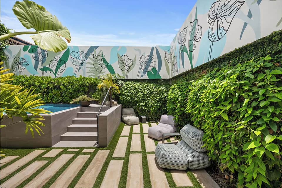 Modern poolside patio with concrete sun loungers, tropical plants, and botanical wall mural