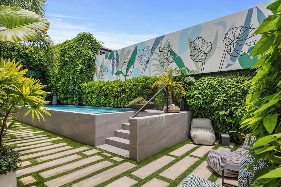Elevated modern swimming pool surrounded by lush green landscaping and botanical wall art
