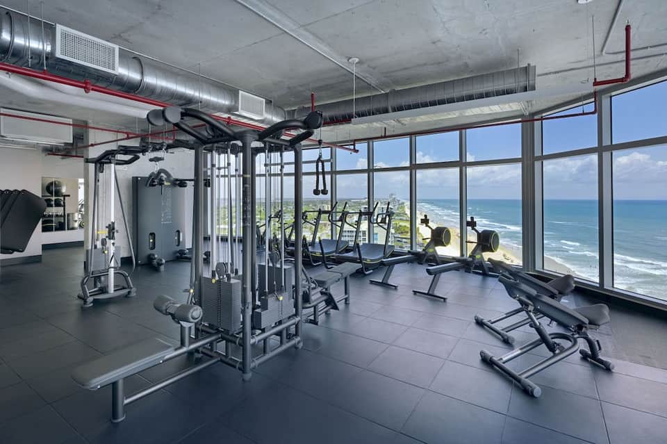 Contemporary gym with cardio equipment and expansive ocean and coastal views through large windows