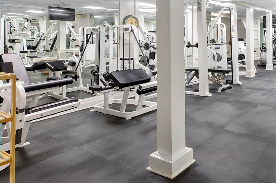 Spacious fitness center with white exercise equipment, machines, mirrors, and bright fluorescent lighting