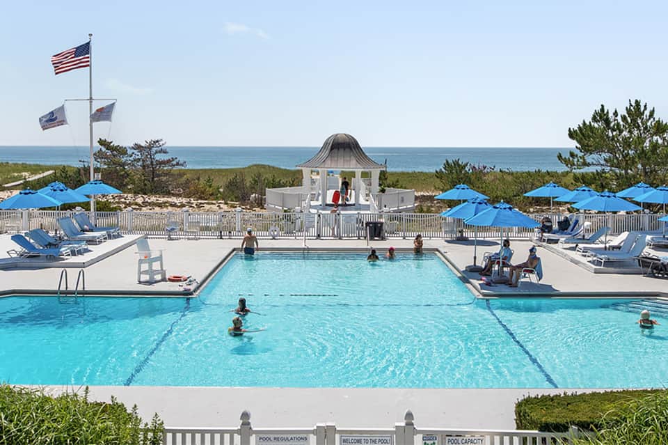 Beachfront pool with swimmers, blue umbrellas, and ocean view
