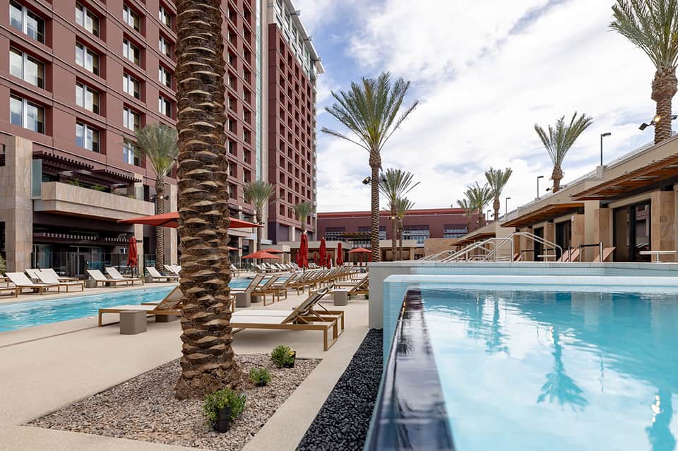 Resort pool area with palm trees, lounge chairs, and multi-story brick buildings