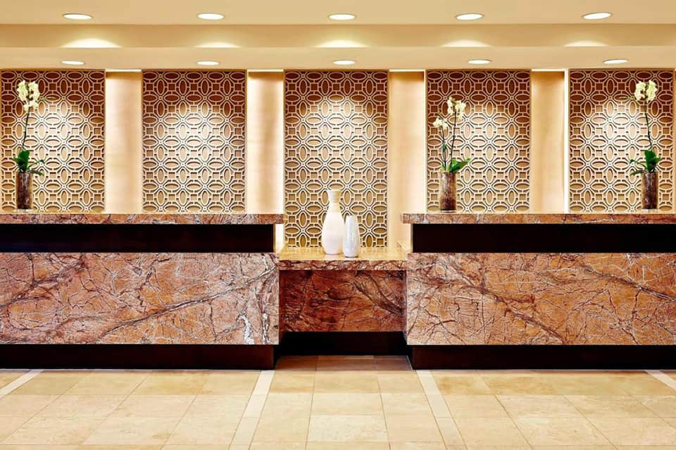 Hotel reception desk with marble countertop, ornate geometric wallpaper, recessed lighting, and fresh flowers