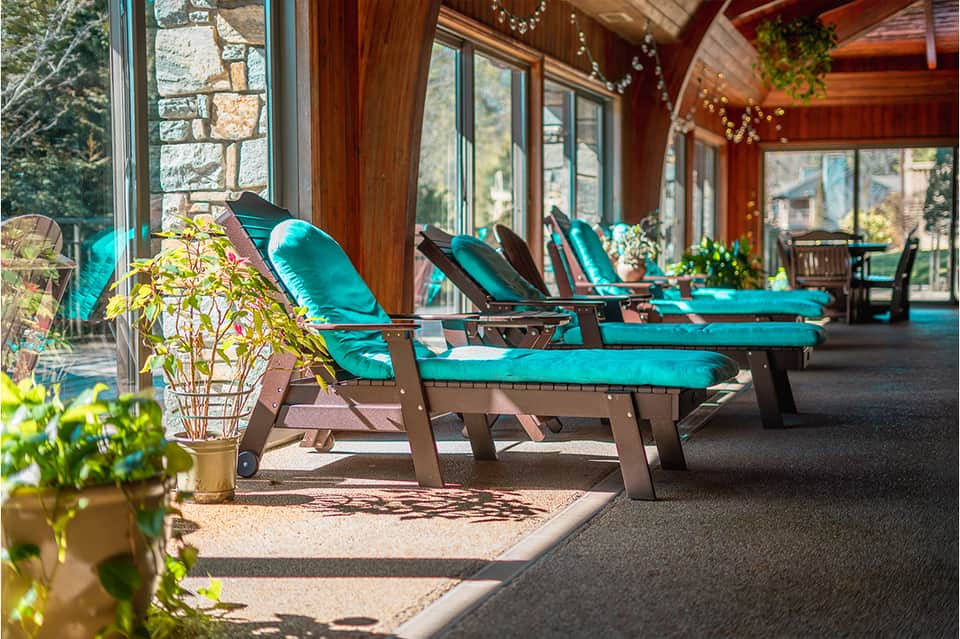 Spa relaxation area with turquoise loungers, large windows, wooden beams, and garden views