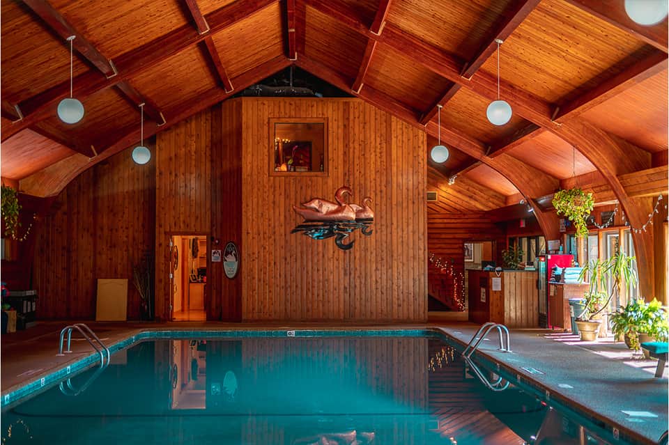 Indoor pool facility with exposed wooden beams, turquoise water, and rustic wooden architectural details