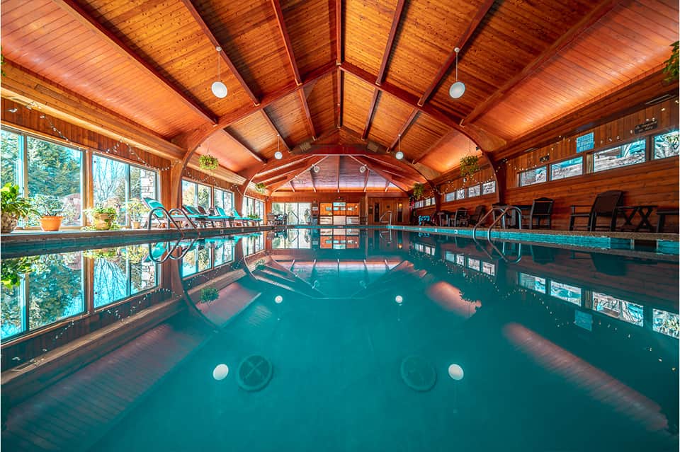 Indoor wooden pool facility with high arched ceiling, windows, and lounge chairs