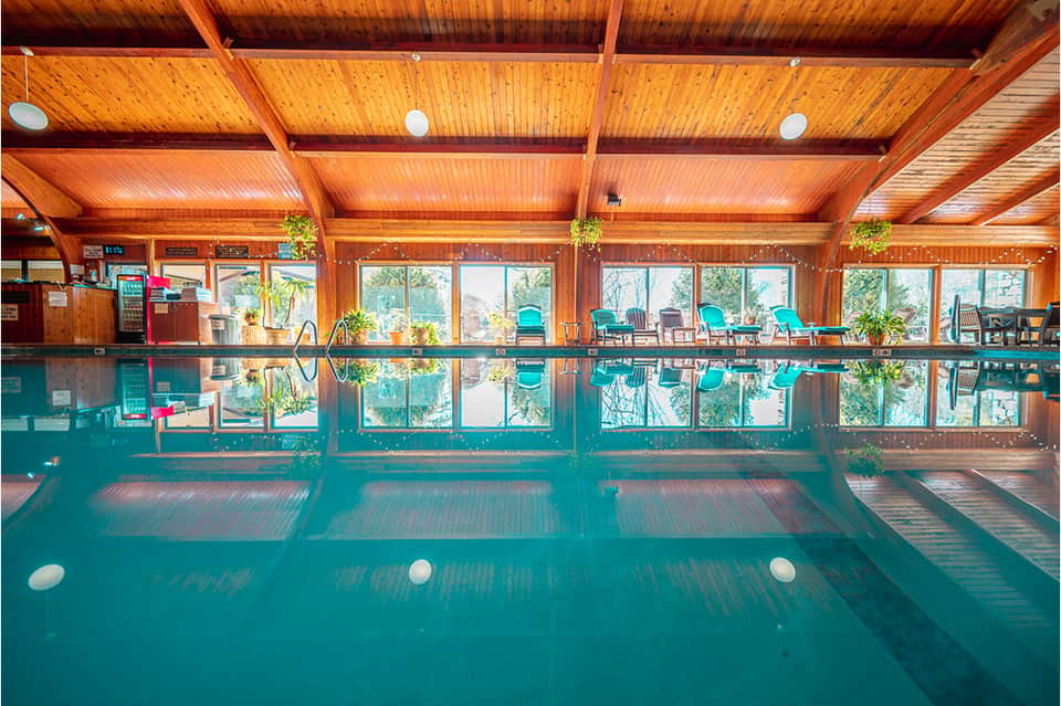 Indoor thermal pool with wooden ceiling, large windows, and lounge chairs overlooking scenery