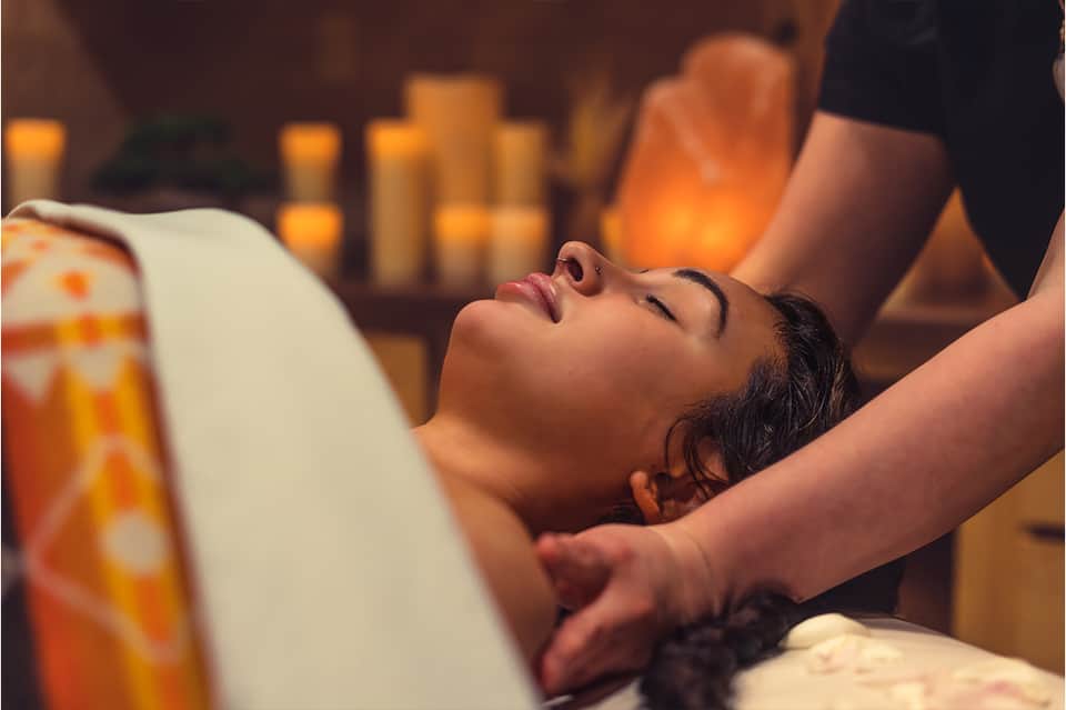 Spa treatment room with person receiving head massage by candlelight with warm ambiance