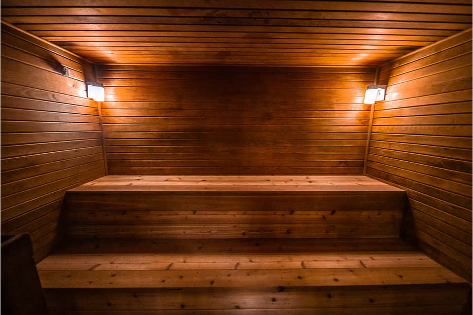 Wooden sauna interior with bench seating, ambient lighting, and horizontal wood paneling