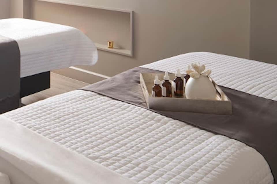 Minimalist spa treatment beds with white linens and amenity bottles