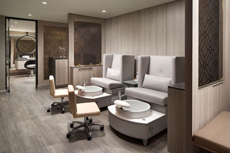 Modern spa pedicure station with white basin chairs, neutral tones, and geometric wall panels