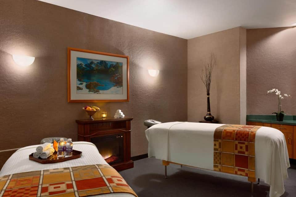 Spa treatment room with two massage beds, warm lighting, and decorative artwork