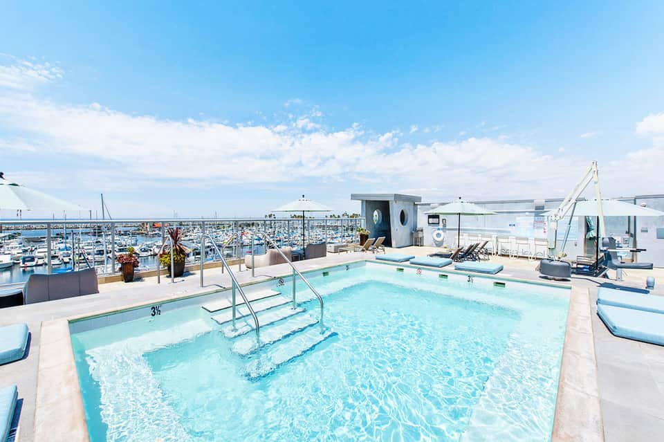 Turquoise swimming pool with steps on a rooftop overlooking a marina filled with boats