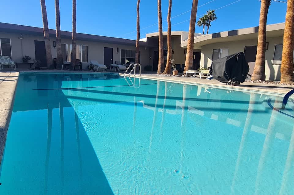 Rectangular swimming pool with palm trees and modern mid-century motel rooms