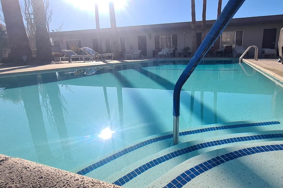 Lap pool with lane markings, blue ladder, and loungers visible in bright sunlight