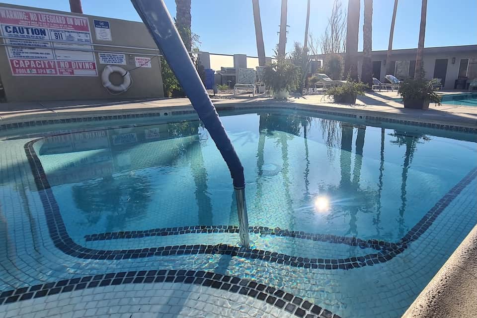 Indoor lap pool with palm tree columns, clear water, and pool safety signage visible