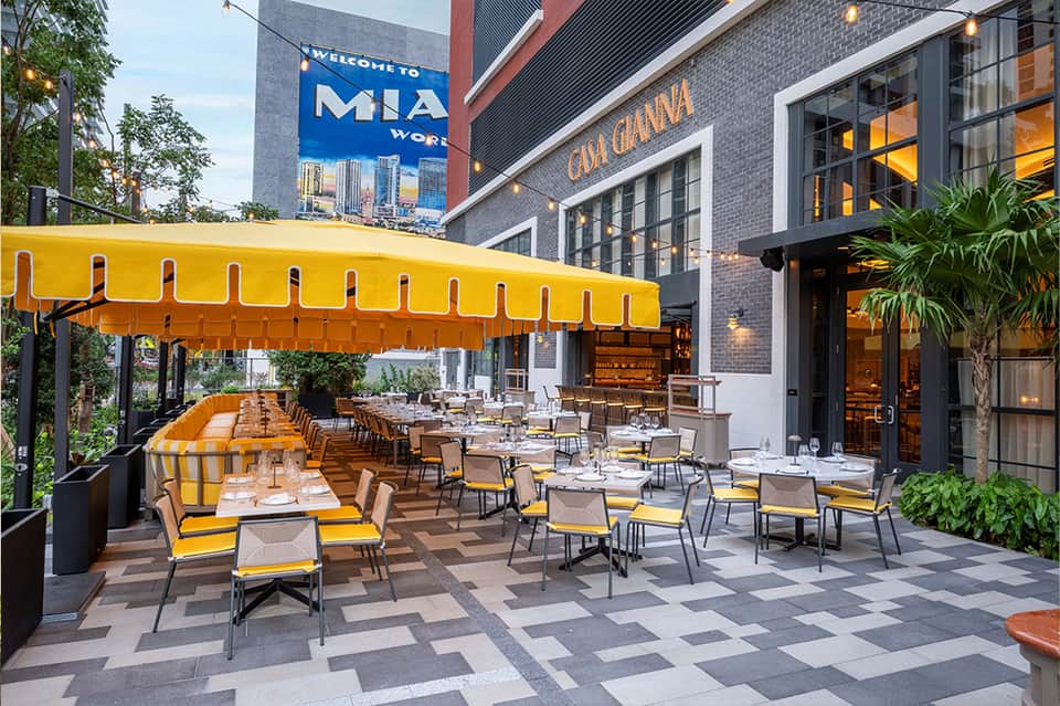 Rooftop restaurant with yellow striped umbrellas, modern furniture, urban skyline view, and Casa Gianna signage