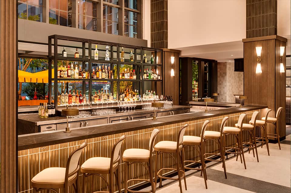 Modern bar with wood paneling, leather bar stools, illuminated shelving, and liquor bottles
