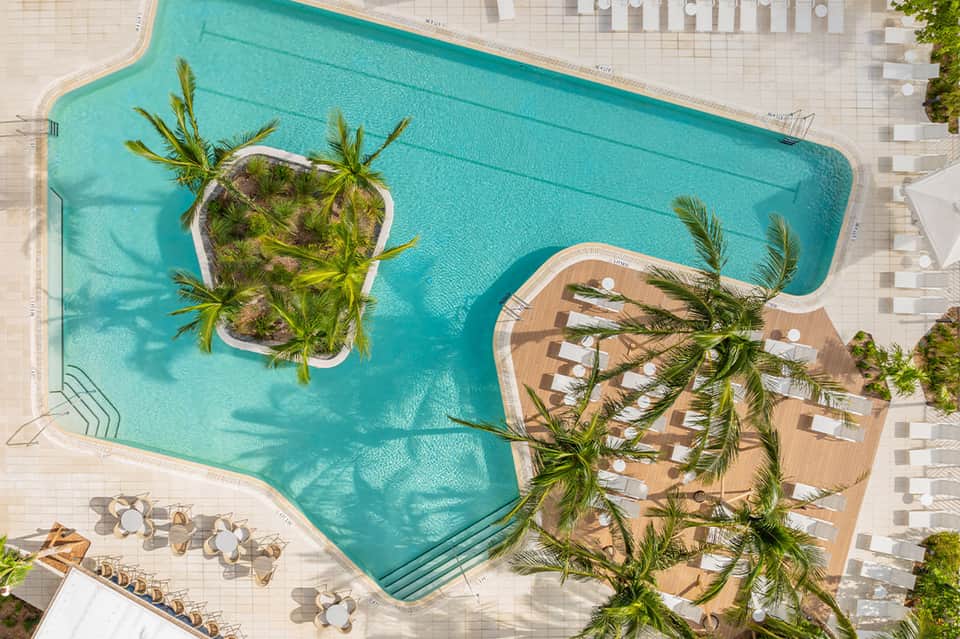 Aerial view of turquoise pool with palm tree islands and wooden deck loungers