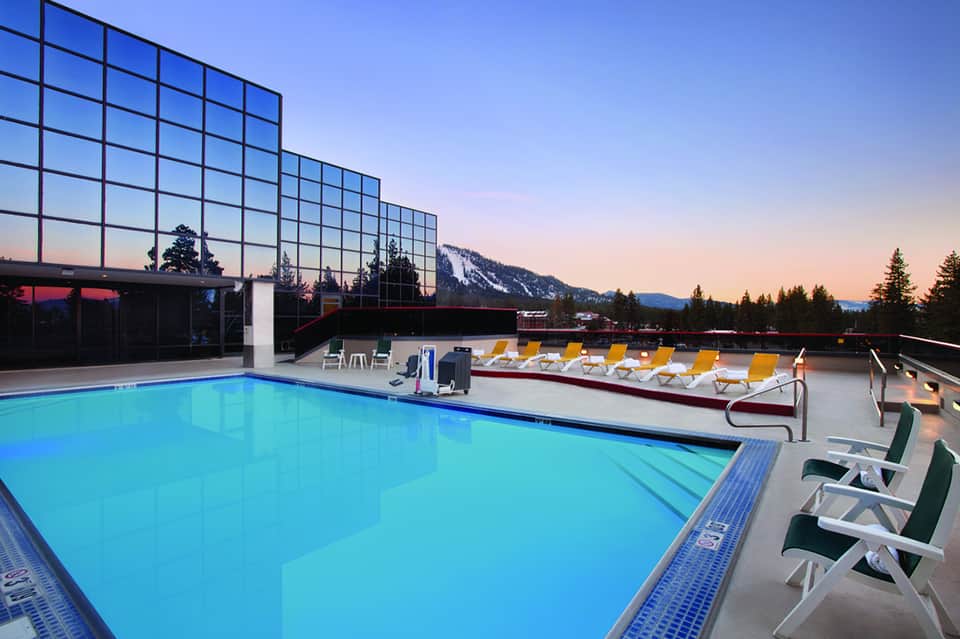 Modern indoor pool with floor-to-ceiling windows overlooking mountains at twilight