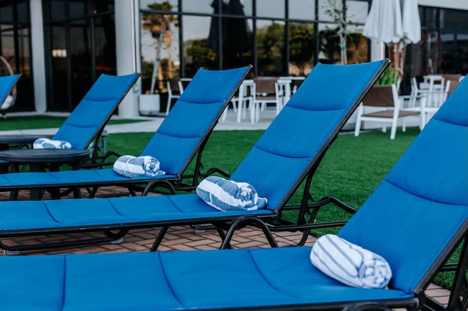 Row of blue chaise lounges with white rolled towels on manicured lawn facing modern building