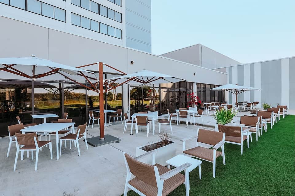 Hotel patio with white umbrellas, lounge seating, fire pit, and manicured lawn