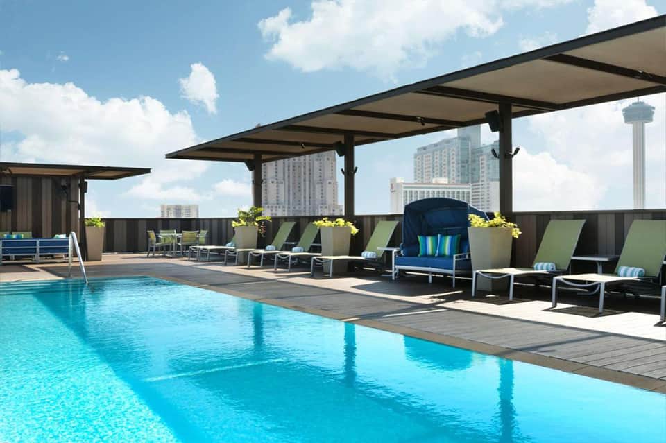 Resort rooftop pool with blue water, lounge chairs, and city skyline in background