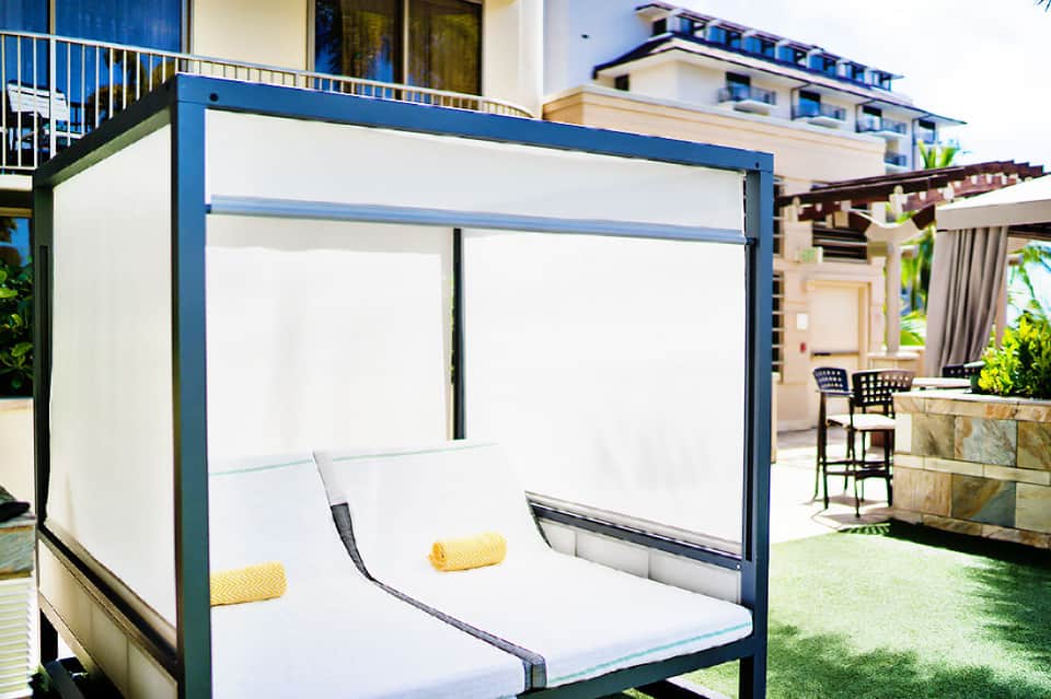 Modern blue and white canopy bed on resort patio with ocean view and palm trees