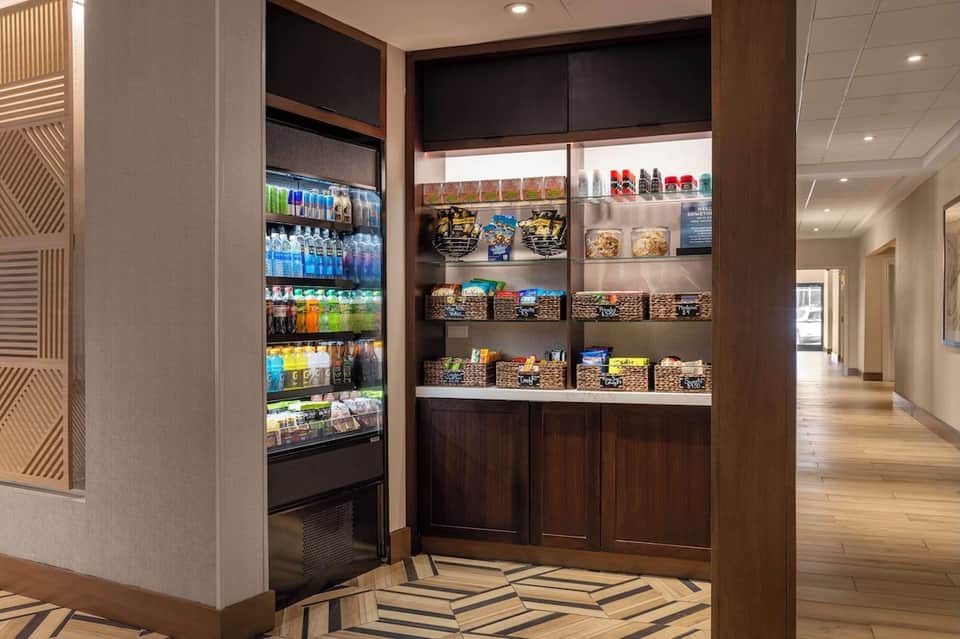 Modern hotel snack bar with refrigerated beverage display and woven basket storage shelving