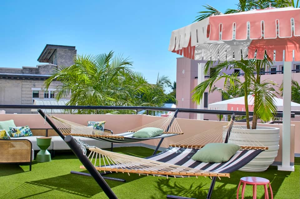 Rooftop lounge with striped hammocks, palm trees, pink building architecture, and colorful accent tables