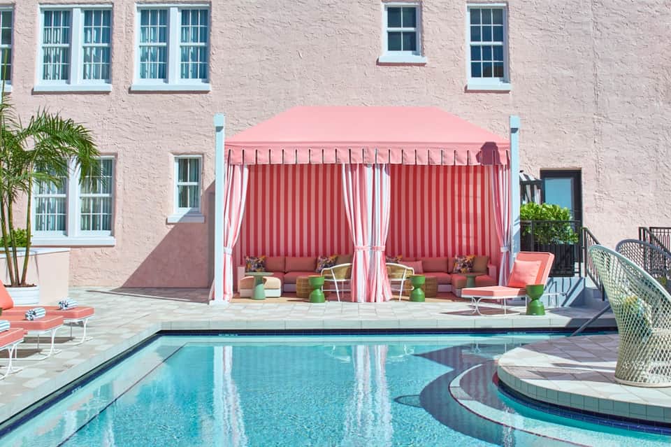 Poolside cabana with pink striped curtains, lounge seating, and pink-themed pool area
