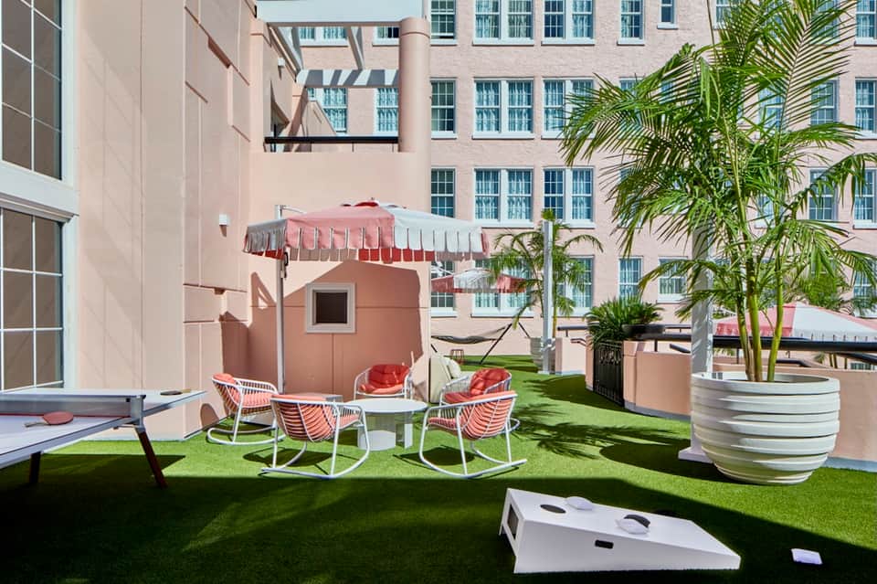 Modern resort rooftop lounge with white chairs, coral umbrella, and manicured grass